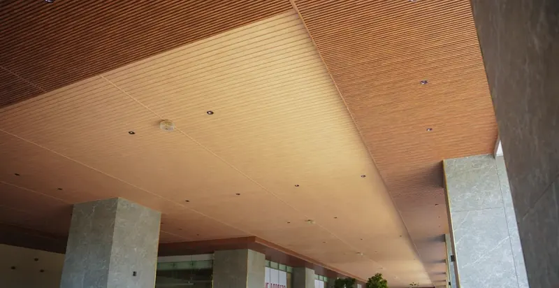 Timber WPC linear ceiling over a commercial porte-cochère with marble-clad columns
